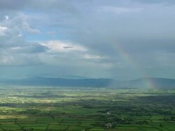 Aerial wide shot rain clouds and rainbow over green landscape / County Cork, Ireland Stock Footage