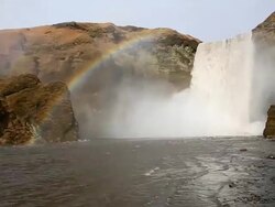 MS PAN View of waving river and rainbow appearing over Skogafoss Falls with Large quantities of water falling in to basin of Skogafoss Falls from top of cliff / Iceland Stock Footage