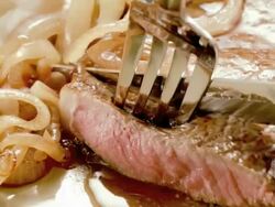 ECU steak knife cuts a slice from cooked sirloin steak as fork lifts slice from sirloin steak served on a plate with mashed potatoes and onions  Stock Footage
