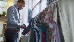 Shop employee tags shirts in modern clothing store with tagging gun Stock Footage
