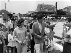 B/W 1961 John + Jacqueline Kennedy walking on pier followed by people / Hyannis Port Stock Footage