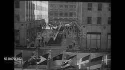 1943: ROCKEFELLER PLAZA EXHIBIT: HD: HA LS (Facing 5th Avenue) United Nations Exhibition in the Channel Gardens sponsored by the United States Office of War Information (OWI), people walking between buildings, UN Member country flags flying below. Instructional Video