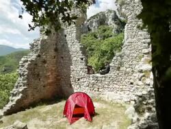 Hiker relaxes on stone wall while writing journal, beside tent Stock Footage