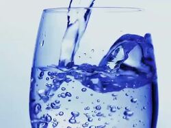 CU TU SLO MO Shotof Sparkling water being poured into glass against blue background / Calvados, Normandy, france Stock Footage