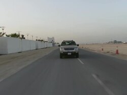 MS TS Car turns corner near some low residential buildings and travels along a masonry wall and under archway and out through gates / Doha, Qatar   Stock Footage