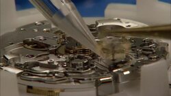 Tweezers drop components onto a partially assembled watch with spinning gears at a watchmaking factory. Stock Footage
