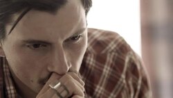 Young man broods on motel bed as young woman paces in background Stock Footage