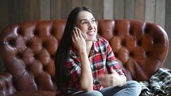 Young beautiful woman talking on a smartphone while sitting on a sofa Stock Footage