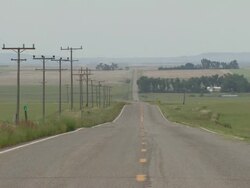 Straight road across prairie and farm land. Road dissapears on distant horizon, USA Stock Footage