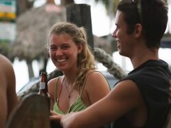 three people sitting at a table talking and drinking beers in swimsuits Stock Footage