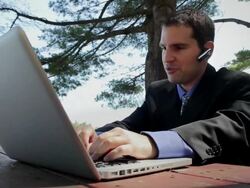 MS Man sitting on table and talking on bluetooth while typing on laptop near lake / Portland, ME, United States Stock Footage