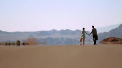 Young couple walk down a desert road in the sweltering heat Stock Footage