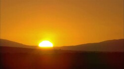 A molten sun sinks behind a mountainous horizon. Stock Footage