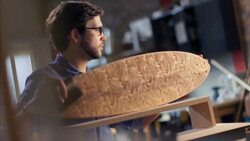 Young artisan runs hand along smooth curve of wooden longboard in workshop Stock Footage