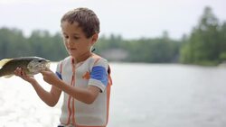 Young boy holding fish he just caught from lake Stock Footage