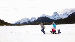 Family sledding in snowy field below mountains Stock Footage