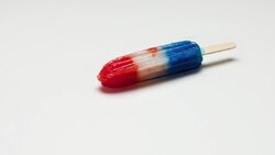 'A red, white and blue ice pop melts on a white surface.' Stock Footage