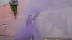 Cool young woman with purple mohawk practicing martial arts spinning kick with purple powder cannon in urban parking lot Stock Footage