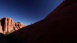 Wide shot of hikers in silhouette hiking on steep desert trail with red-rock mountains in background in Utah (pan) Stock Footage