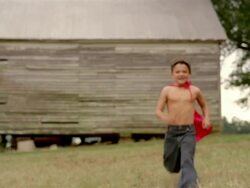 Long shot shirtless boy wearing a red cape running towards CAM / flexing muscles and making a face Stock Footage