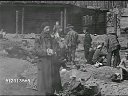 1940s: CONCENTRATION CAMP: GRAPHIC FOOTAGE: HOLOCAUST: PAN Camp yard w/ emaciated men in stripped uniforms. CU Emaciated starving Jewish male. MS Two emaciated starving men sitting on ground. Man in stripped clothing by fire. Two men lying by fence. Instructional Video