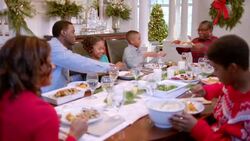 Family pass plates around table for Christmas dinner, cute young girl smells sweet potatoes hungrily as father serves them (dolly-shot) Stock Footage