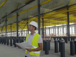 WS PAN engineer holding plan standing in large hangar, looking around ostensible checking things, front view, RED R3D 4K Stock Footage