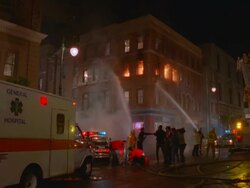 WS Firemen spraying water on corner of four story brick apartment building / Unspecified Stock Footage