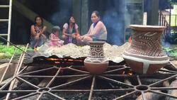 Wide shot of Kichwa Indian women and child as they oversee the firing of traditional, hand-made ceramic pottery on an open fire in the Ecuadorian Amazon. Stock Footage