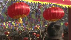 Devotees pass beneath red silk lanterns and colorful pennants hanging outside White Cloud Temple. Stock Footage