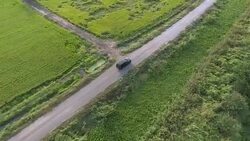 Aerial: Black SUV car driving along green fields Stock Footage