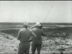 1942: FORT JACKSON REVIEW: VS British Prime Minister Winston Churchill (1874-1965) w/ portable transistor radio watching US Army parachute infantry paratroopers landing in field,  Brigadier General William C. Lee (1895-1948) beside.  WWII, airborne Instructional Video
