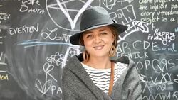 Elegant young woman standing in front of a black board filled with scribbles and looking at camera Stock Footage