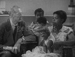 1953: WELL-BABY CLINIC: Dr. Spock in room talking (No SOT) w/  African-American mother w/ baby in cloth diapers standing in lap, young boy, brother standing BG. Instructional Video