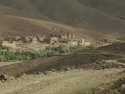 A light breeze moves the palm trees that sit by an old style settlement, amongst the Moroccan hills. Stock Footage