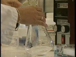 CU Hands pouring clear liquid into flask Stock Footage
