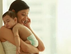 Woman carrying her sleeping baby and talking on mobile phone Stock Footage