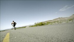 Young skater speeds down empty desert road and bails off skateboard (slow-motion) Stock Footage