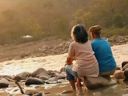 Rear view of a senior couple sitting at riverbank, Ganges River, Rishikesh, Uttarakhand, India Stock Footage