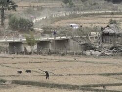 WS truck driving over bridge and farmer walking through field / Xam Neua, Laos Stock Footage
