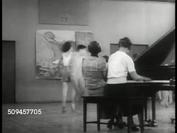 1936: U.S. MIDDLE SCHOOL: BALLET CLASS: WS Female teachers at piano, middle school children dancing BG. MS Children dancing ballet in large circle. WS Children dancing in circles, art painting BG. Dance class Instructional Video
