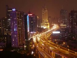 TL of highway with busy traffic between high rise buildings in Shanghai at night. Slight Zoom in. Stock Footage