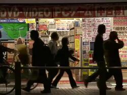 MS Shot of manga comic shop in Tokyo with pedestrians and traffic passing in front of it at night / Tokyo, Japan Stock Footage