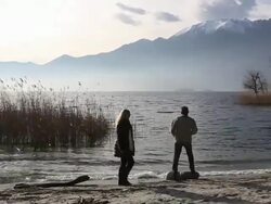 Pan as couple walk along mtn lake edge, stop to take picture Stock Footage