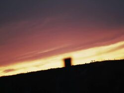 Silhouetted windmill and trees in front of a cloudy sky at sunset Stock Footage