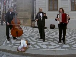 Medium shot trio of muscians performing on the street / man walking past putting money in hat / Prague Stock Footage