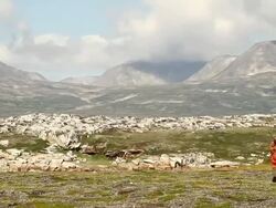 WS PAN View of hunter walking towards mountains and rocky fields with blue sky / Torgat Mtns, Labrador, Canada Stock Footage