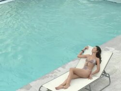 Young woman in sunlounger by pool, young man swimming in pool then sitting poolside Stock Footage