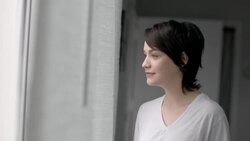 Young woman stares out bedroom window drinking coffee, looks back at boyfriend in bed and smiles Stock Footage