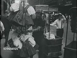 1963: NEW YORK CITY GARMENT DISTRICT:  Man pushing rack of 'Junior' clothing, dresses down sidewalk. Racks of clothing being pushed, moving up sidewalk.  Iconic, fashion, design, Chelsea neighborhood, 1960s. Instructional Video